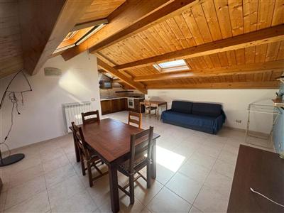 Mansarda: cucina abitabile con tavolo da pranzo, divano e soffitto in travi di legno